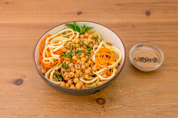 Vegan salad with zucchini noodles, carrot noodles, cooked chickpeas, olive oil, chopped parsley, and sesame poppy seeds in a black bowl