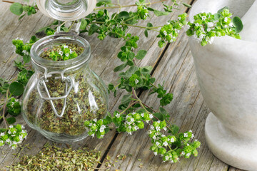 Dried Oregano on a jar over a wooden table with mortar and branches with flowers around it