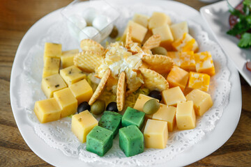 On the table is a plate with cheese, crackers, olives and nuts