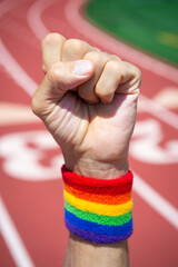 Athlete wearing gay pride rainbow wristband punches the air in front of a sports track background - 445797979