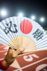 Hand of Japanese sports athlete standing outdoors holding a fan decorated with kanji characters...