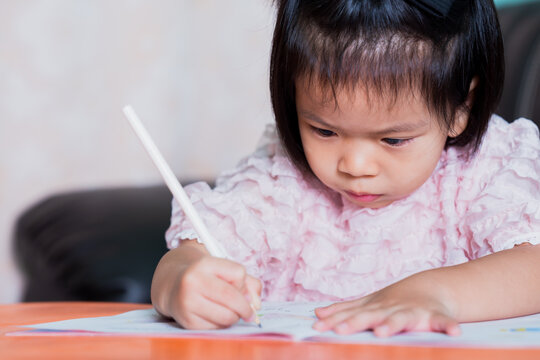 Adorable girl holding pencil with light hand. Child writing on the book intentionally. Kid aged 4-5 year old.