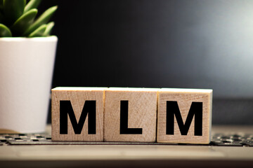 MLM Multi-Level Marketing written on a wooden cube in a office desk.