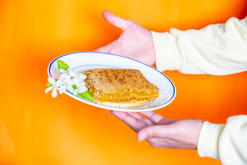 Hands holding a white rose with honey in the same bowl with orange background