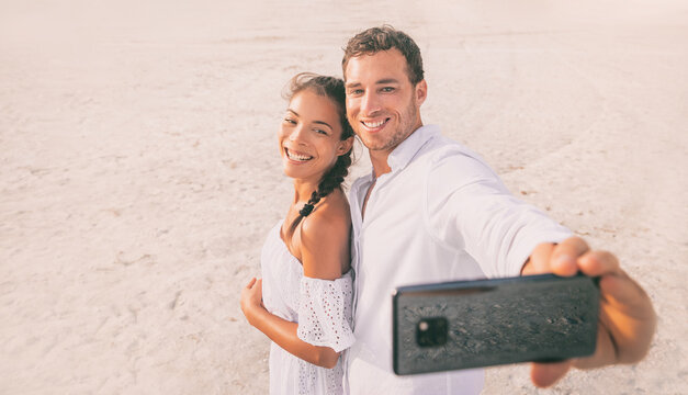 Phone selfie photo portrait couple happy on summer vacation travel tropical caribbean beach destination taking mobile phone picture of honeymoon.