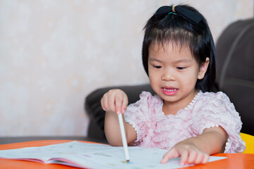 Asian girl doing homework. Cute child held a white pencil and pointed suspiciously at her book....