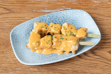 Skewer of fried aubergine tacos battered with cheese sauce on a blue plate and chopped chives on a wooden table