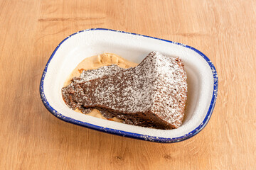 Portion of brownie cake with chocolate ice cream and icing sugar on top on an enameled metal container
