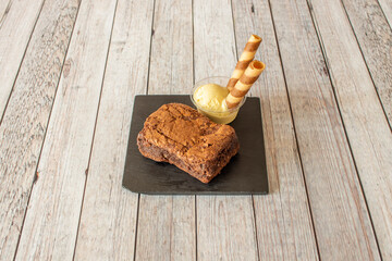 Ration of chocolate brownie cake with vanilla ice cream and biscuit wafer on black slate plate