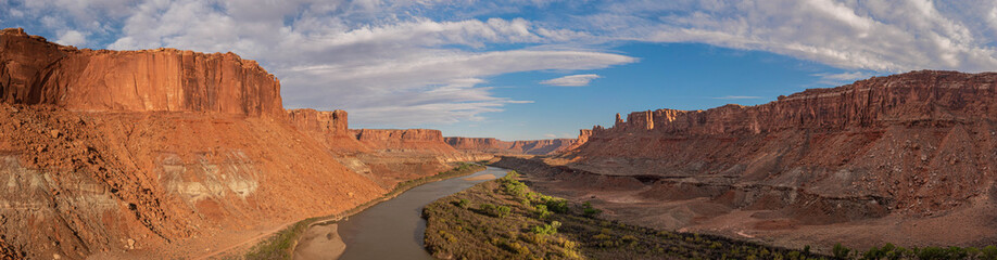 Aerial panorama in of Canyonlands National Park looking south over the Green River into the orange canyons with partly cloudy skies and evening light.