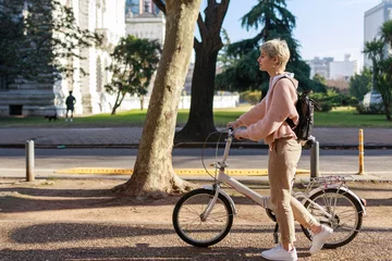 Foto op Plexiglas young woman walking down the street of the city. She is carrying a backpack on her back and bicycle with her hands. Profile view. Horizontal plane. Copy space for text on left side. © Ri Fotoproducto