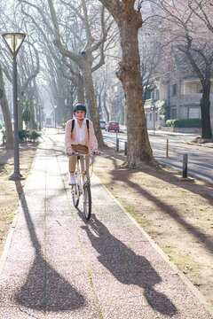 young woman rides a bicycle on street boulevard of the city, a sunny autumn day. She wears a safety helmet. Concept of health care and environment. Vertical image with copy space for text.