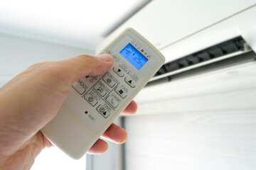 Man's hand using remote control open The air conditioner is cooled to 25 degrees Celsius in his bedroom. Health concepts and energy savings