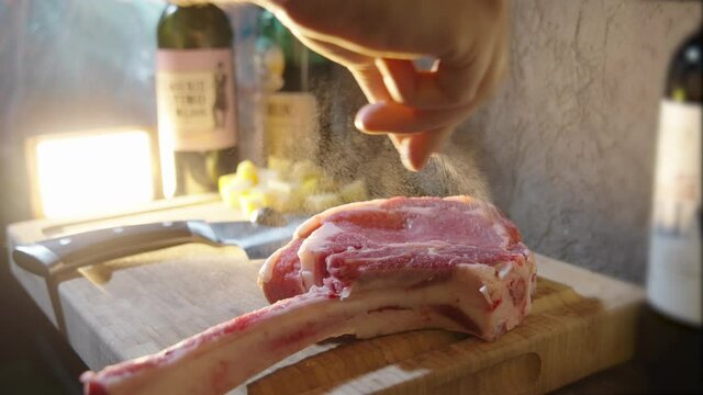 Man rests a raw Tomahawk firmly on a table to salt it
The cut of meat is reddish and thick