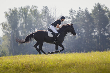 portrait of rider man and black stallion horse galloping during eventing cross country competition...