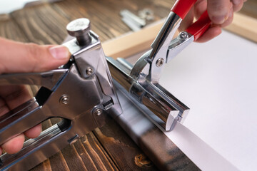 The process of stretching a synthetic canvas onto a stretcher. Hand with stapler and forceps