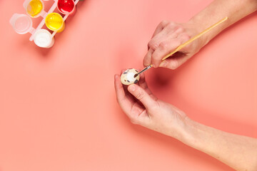A girl paints eggs for Easter pink background