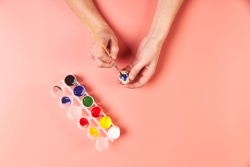 A girl paints eggs for Easter pink background