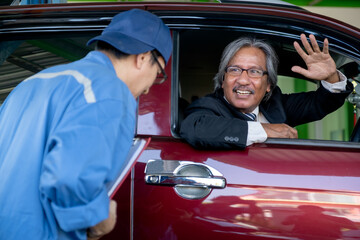 Automotive technician bow to senior customer sit in car and smile after finish fix the problem in shop.