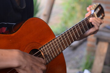 Close-up view of young man playing acoustic guitar while sitting on sofa in home recording studio. Close-up of Young hands playing guitar on blurred background. Recording electric acoustics