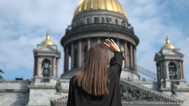 a woman stands with her back and waves her hand at St. Isaac's Cathedral