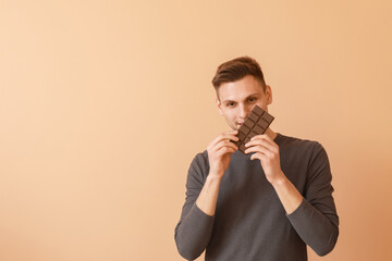 Handsome young man with tasty chocolate on color background