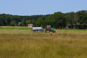 Tractor with manure tank drives in the meadows on a sunny summer day in July. Dunes in the distance. Netherlands