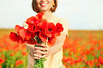 Beautiful young woman with bouquet of poppy flowers in field