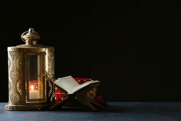 Muslim lantern with Quran and prayer rug on dark background