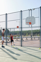 Basketball trainer showing how to shoot basketball to a child with a leg prosthesis. Coach training a kid.
