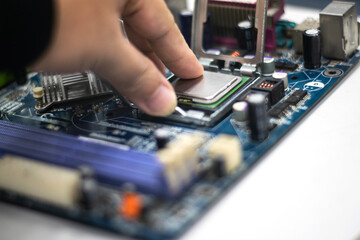 A young man is using his hand to pick up a PC computer CPU on a motherboard with many zips to upgrade a new CPU.