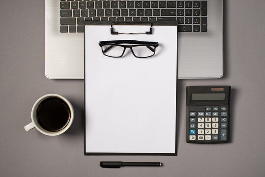 Top view photo of laptop keyboard glasses on black clipboard folder with paper sheet calculator pen and cup of drink on isolated grey background with blank space