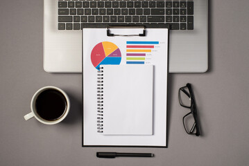 Top view photo of laptop keyboard glasses pen cup of drink and planner on clipboard folder with pie chart diagram on isolated grey background with copyspace