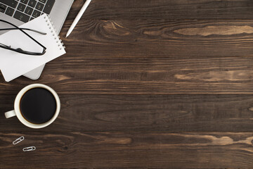Top view photo of glasses small notebook on laptop cup of coffee white pen and clips on isolated dark wooden table background with copyspace