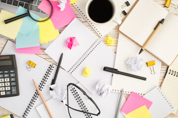 Top view photo of multicolor sticker notes laptop cup of drink binder clips magnifier spectacles notepads pens pencil calculator and crumpled paper balls on isolated wooden table background