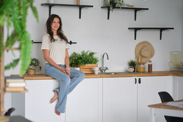 Young beautiful modern woman sitting on counter in the kitchen at home.