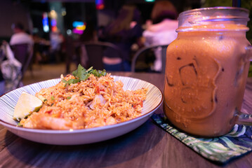 fried rice in a dish with a glass beside it on a restaurant table with neon lights and people in the background