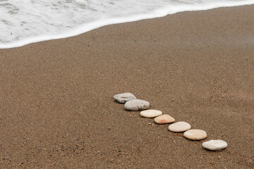 Smooth beach stones in a raw on a sandy coastline and foam of sea water.
