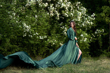 A gentle image of a young woman in a silk green dress with a long train against the background of blooming apple trees.