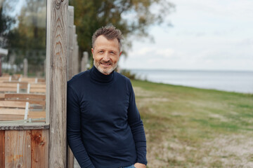 Attractive casual middle-aged man leaning on a wooden post