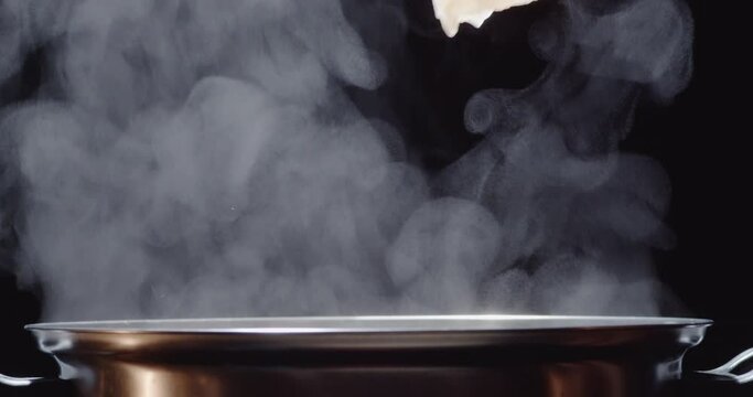 Slow motion of hot pot or shabu-shabu pot made of stainless steel, water boiling, hot steam rising on a black screen, hand using chopsticks to pick up fish pieces into the pot.