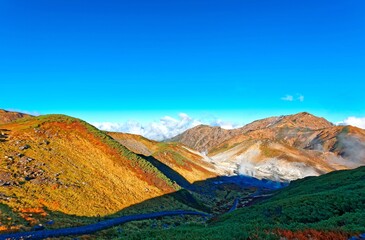 Fototapeta premium Autumn scene of golden grass on the lakeside of Mikurigaike Pond (a volcanic crater lake ) & bright sunlight shining above the mountaintop in Murodo Daira, Tateyama Kurobe Alpine Route, Toyama, Japan