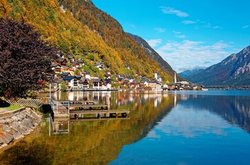 Fototapeta premium Autumn scenery of Hallstatt, an amazing lakeside village in Salzkammergut region of Austria, under blue sunny sky with beautiful reflections on smooth lake water in the brisk colorful fall season