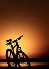 Vertical conceptual photography with a silhouette of a single mountain bike, standing on a sea shore at orange summer dusk