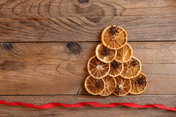 Christmas tree shape made with dried oranges on wooden background, top view. Sustainable Christmas. Traditional Christmas ingredients - orange, cinnamon, star anise. Vintage Christmas decoration.