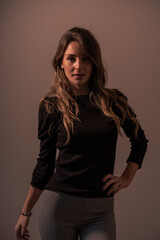 Fototapeta premium Portrait of a young blonde caucasian woman on a brown background with a soft light from the side with looking at camera