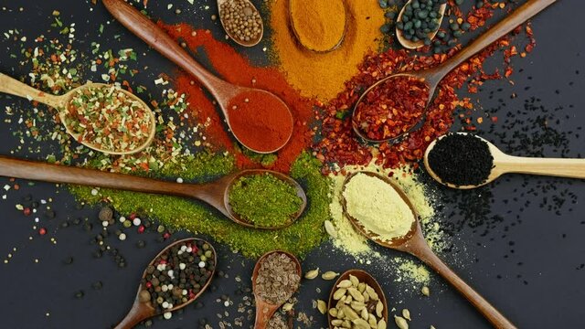 Dry colorful spices in spoons and bowls with fresh seasoning on dark background, top view