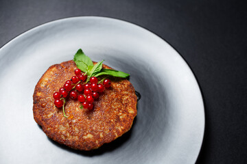 Close-up of vegan homemade pancake with red currants on textured round plate.