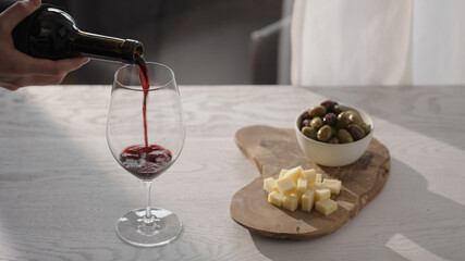 Pour red wine in wineglass with antipasti on white oak table