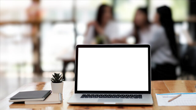 Photo of computer laptop with white blank screen putting on the modern working table with business people having a blurred meeting in the background.